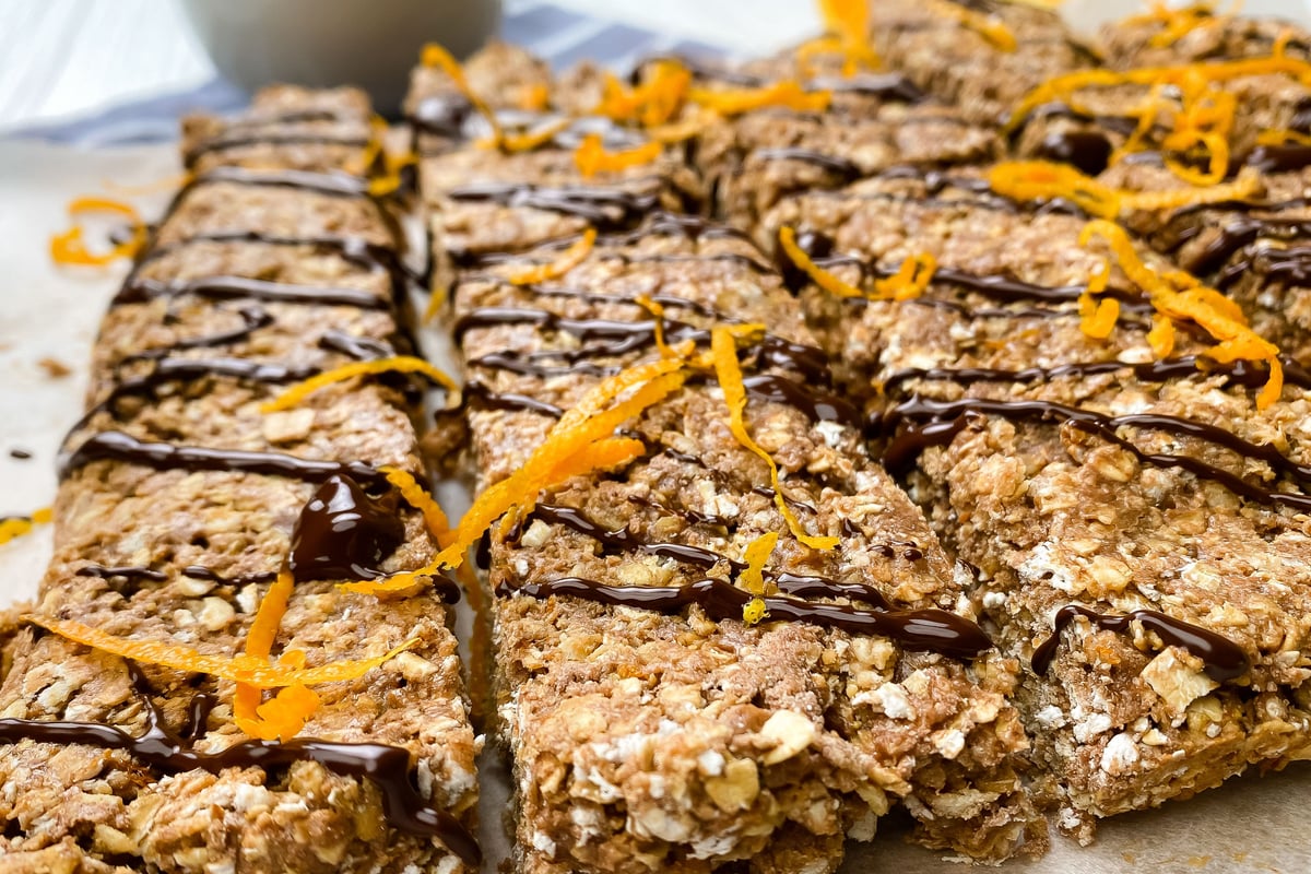 Oat-based protein flapjacks drizzled with dark chocolate and orange zest on white surface