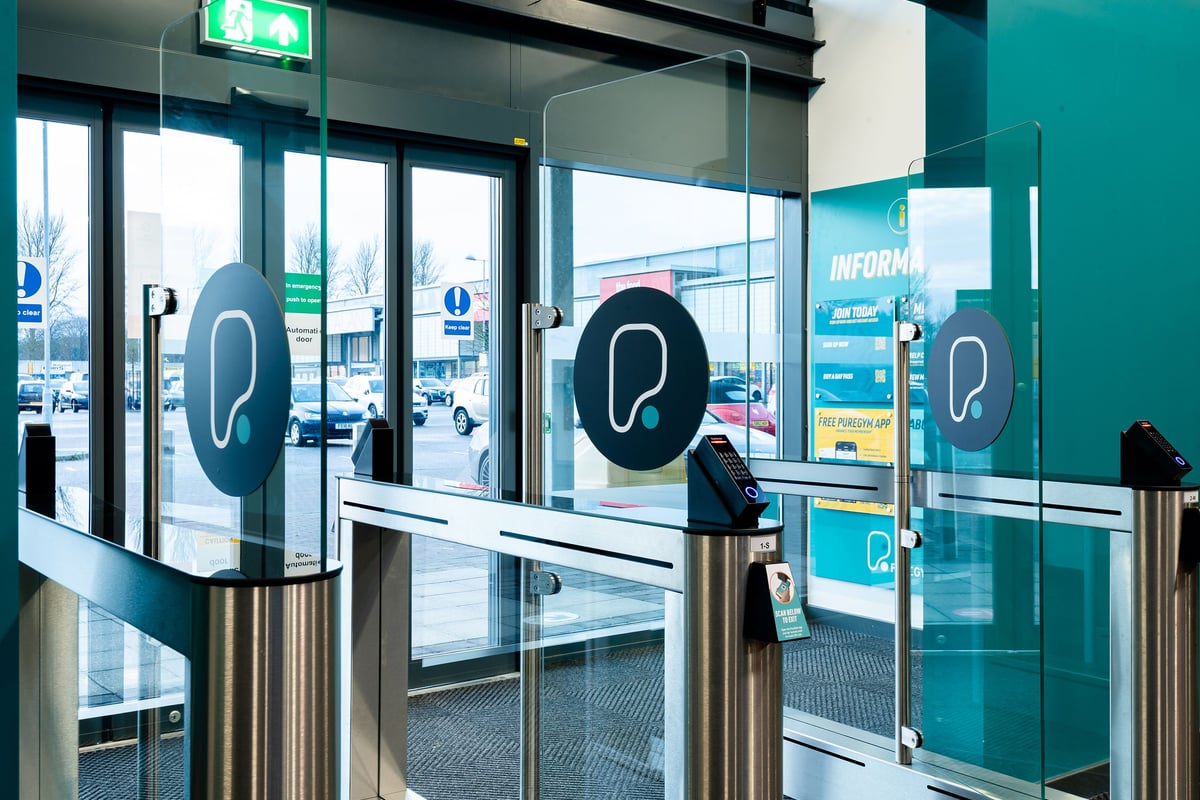 PureGym Elgin: Entrance area with semicircular turnstiles or security gates and informational signage.