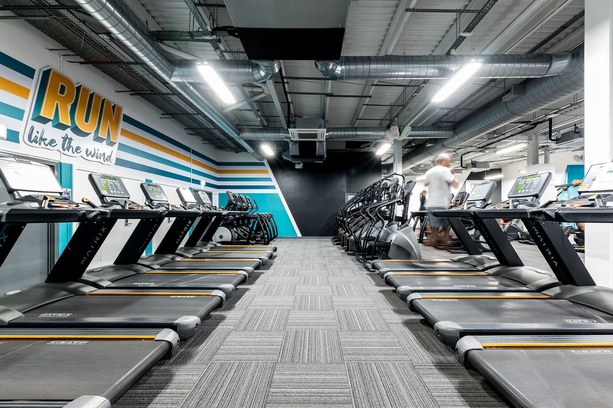 PureGym Cambridge Leisure Park: Rows of treadmills in a well-lit gym with motivational signage along the walls.