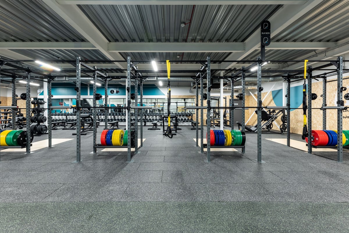 PureGym Eastbourne: Weightlifting rig, squat racks, weight plates, rubberized flooring in a modern gym interior.