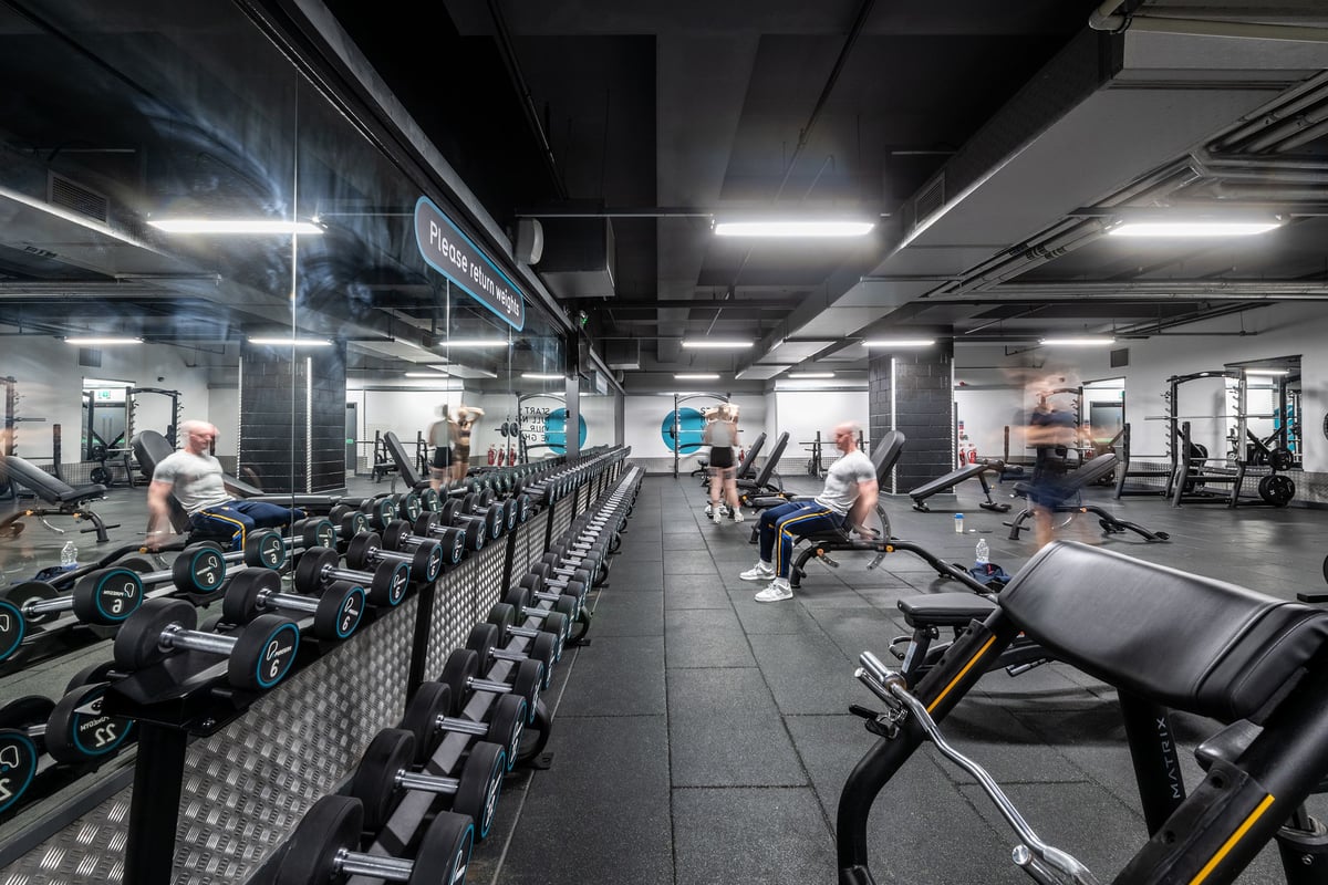 PureGym Liverpool Central: Rows of treadmills, weight racks, benches and blurred human figures in a dimly-lit fitness centre.