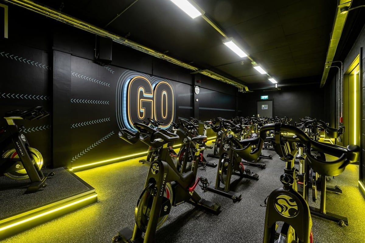 PureGym Milton Keynes Winterhill: Rows of stationary cycles in a dimly lit room with yellow accents and 'GO' signage.