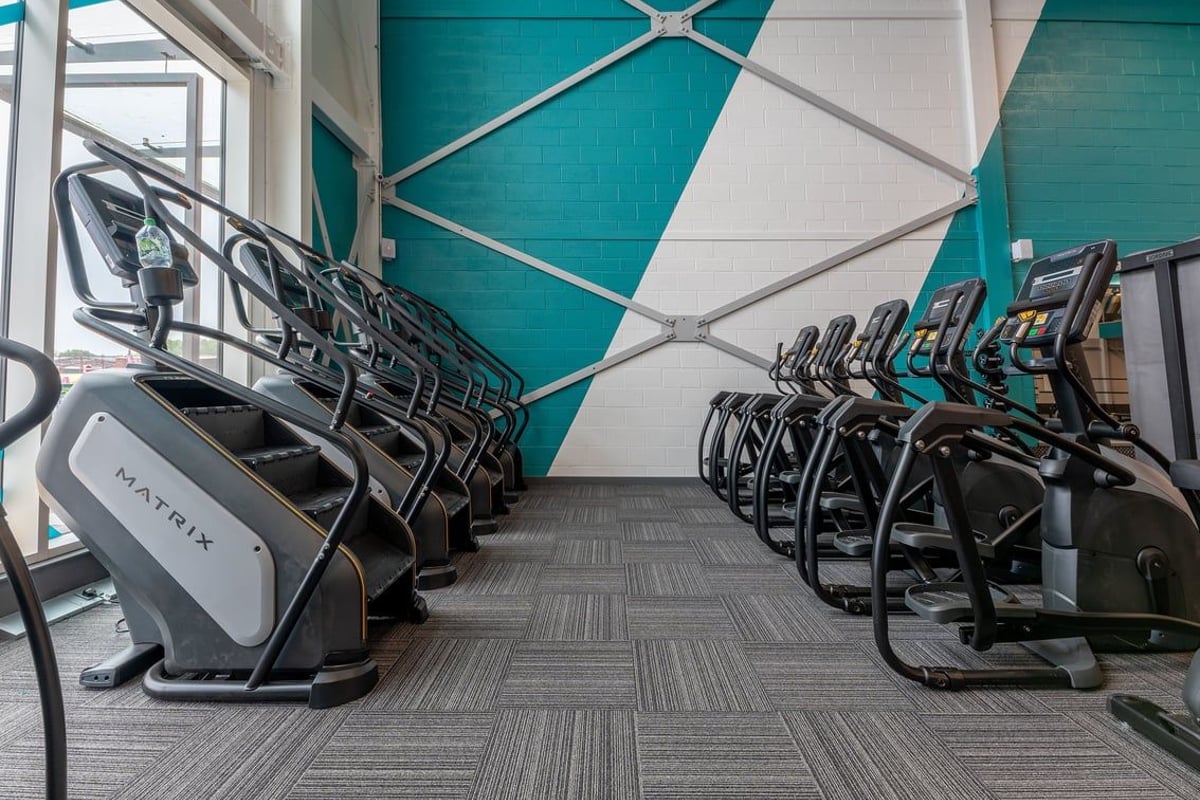 PureGym Liverpool Edge Lane: Rows of elliptical machines and other cardio equipment inside a gym with teal walls.