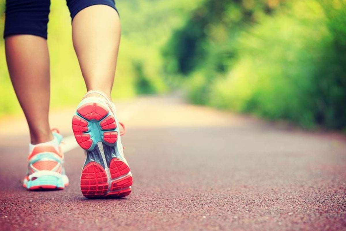 Person walking on a red path surrounded by green trees wearing colourful trainers