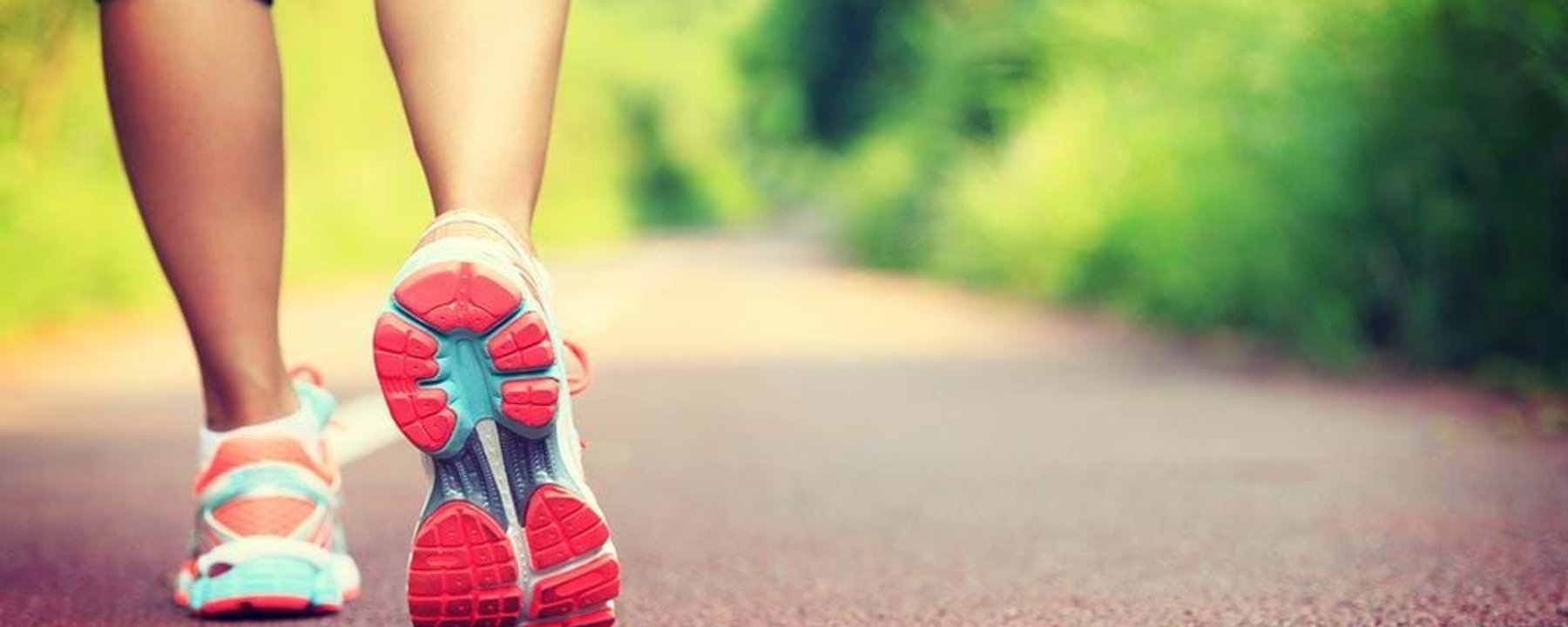 Person walking on a red path surrounded by green trees wearing colourful trainers