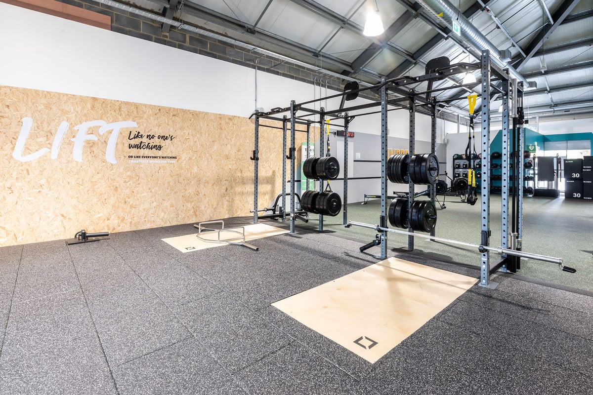 PureGym Stowmarket: Power racks, weight plates, wall graffiti, padded floor, and lifting platform.