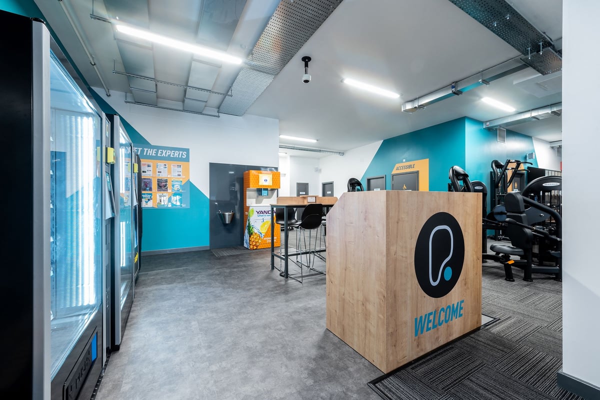 PureGym Coalville: Reception area, high tables, and bright teal accents on the walls.