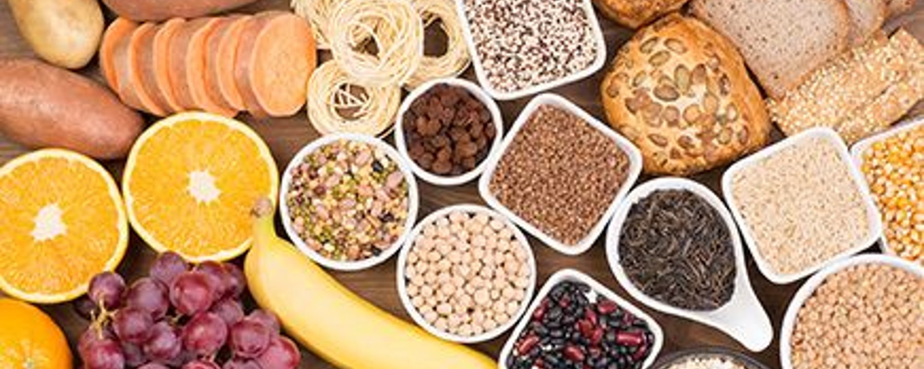 Différents grains entiers, fruits, légumes, noix et pain disposés sur une table.