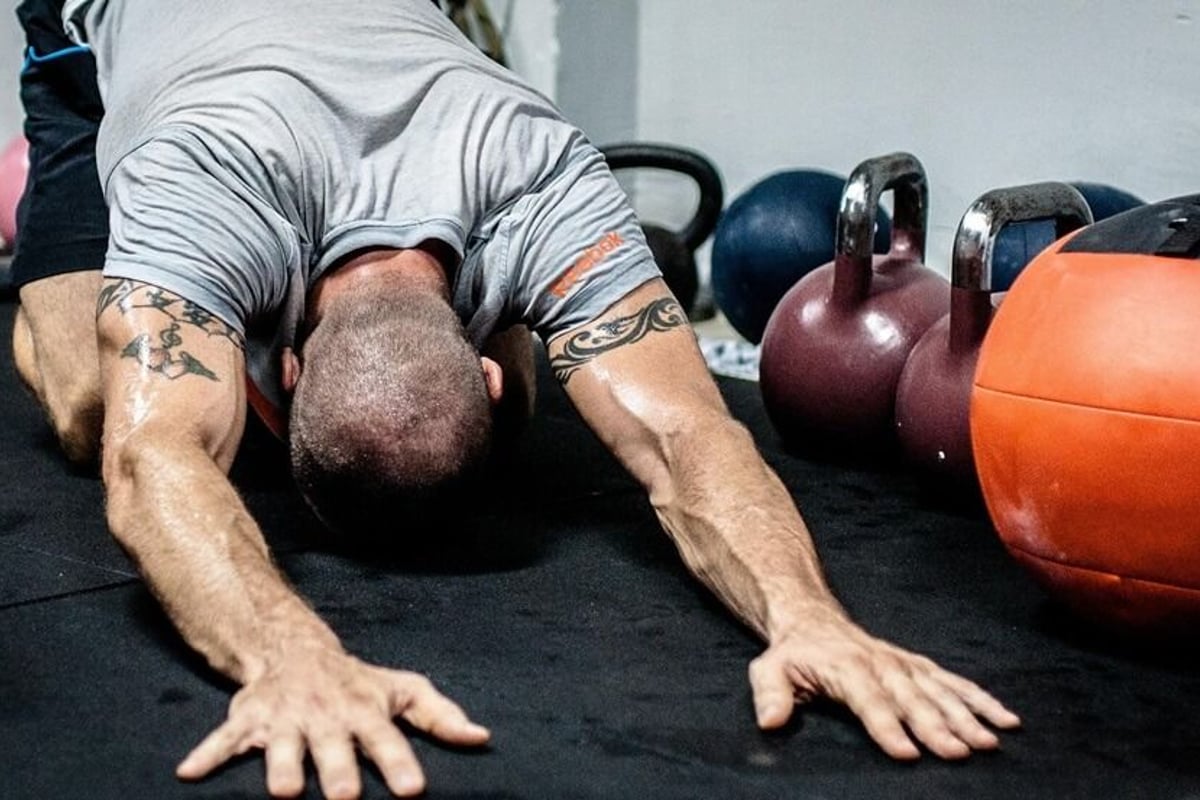Man with tattooed arms performing press-up on gym floor with kettlebells nearby