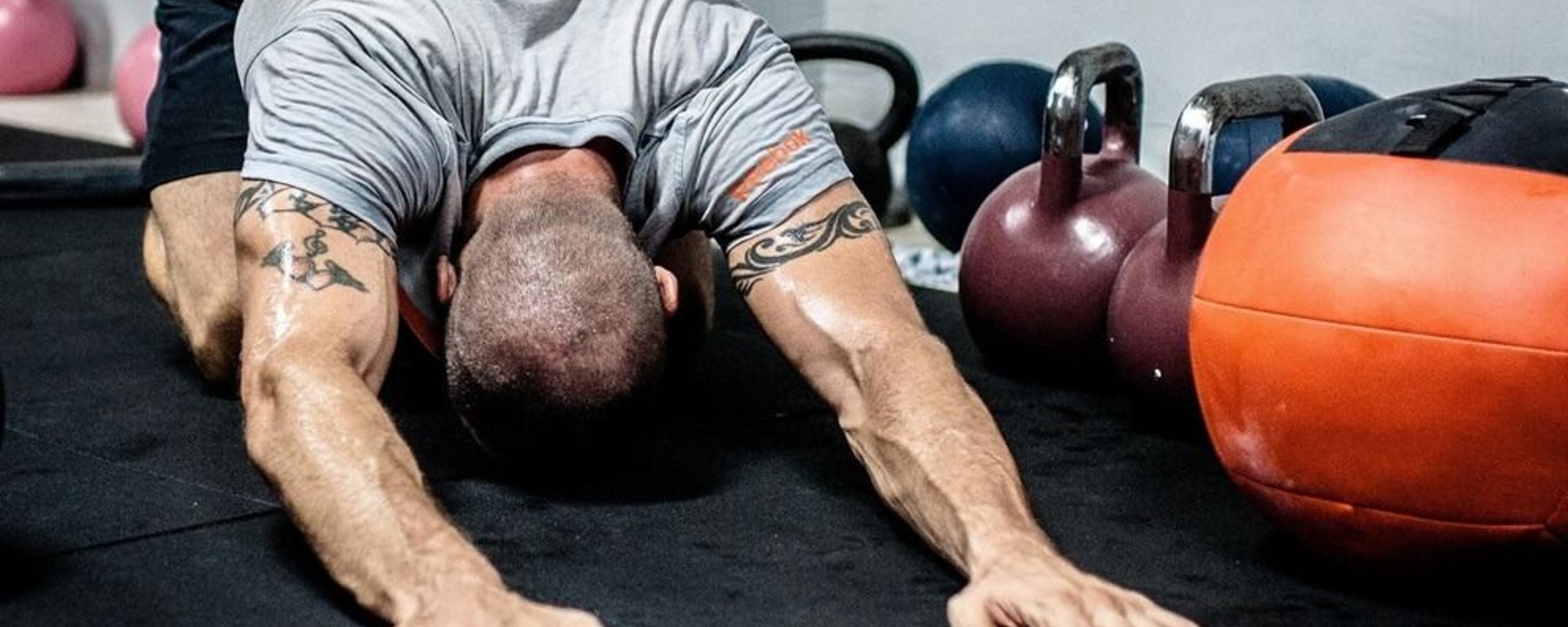 Man with tattooed arms performing press-up on gym floor with kettlebells nearby