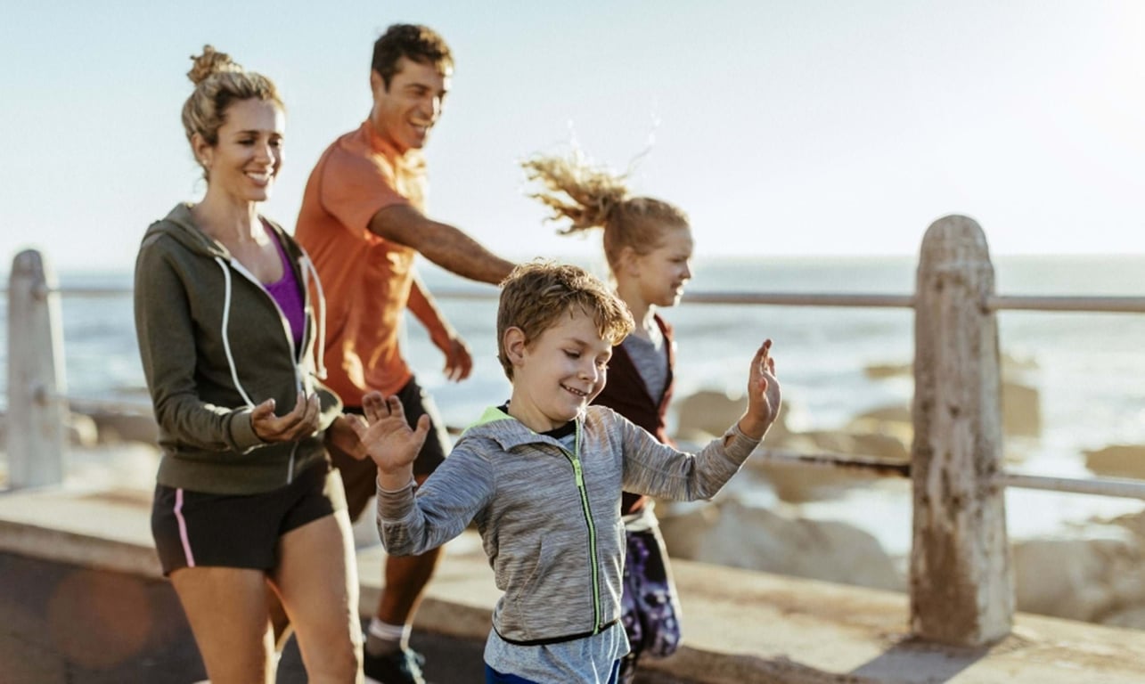 Family of four walking and smiling along a seaside promenade in sportswear