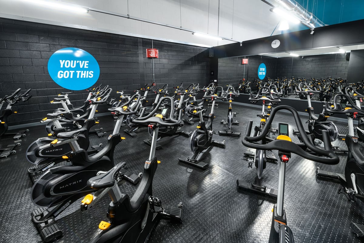 PureGym Cardiff Bay: Rows of stationary exercise bikes fill a dimly lit studio with a motivational sign.