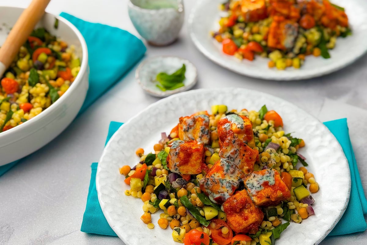 Grilled paneer cubes with mixed vegetable salad and creamy herb dressing on white plates