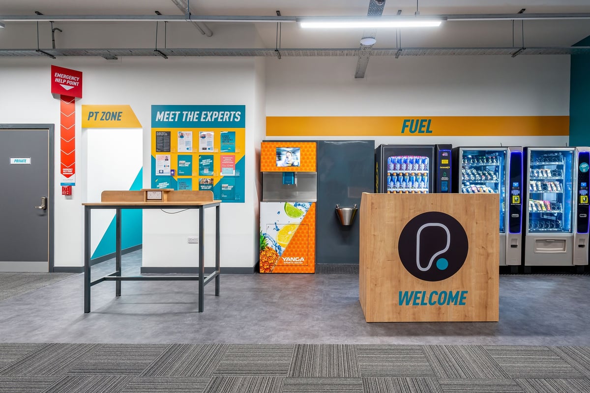 PureGym Stratford-upon-avon: Vending machines, display stands, and a reception counter for what seems to be a retail or service establishment.
