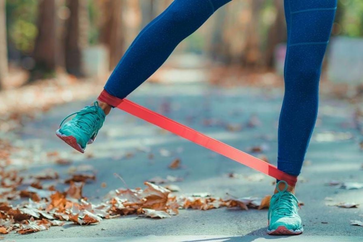Person wearing blue leggings and turquoise trainers exercising with a red resistance band