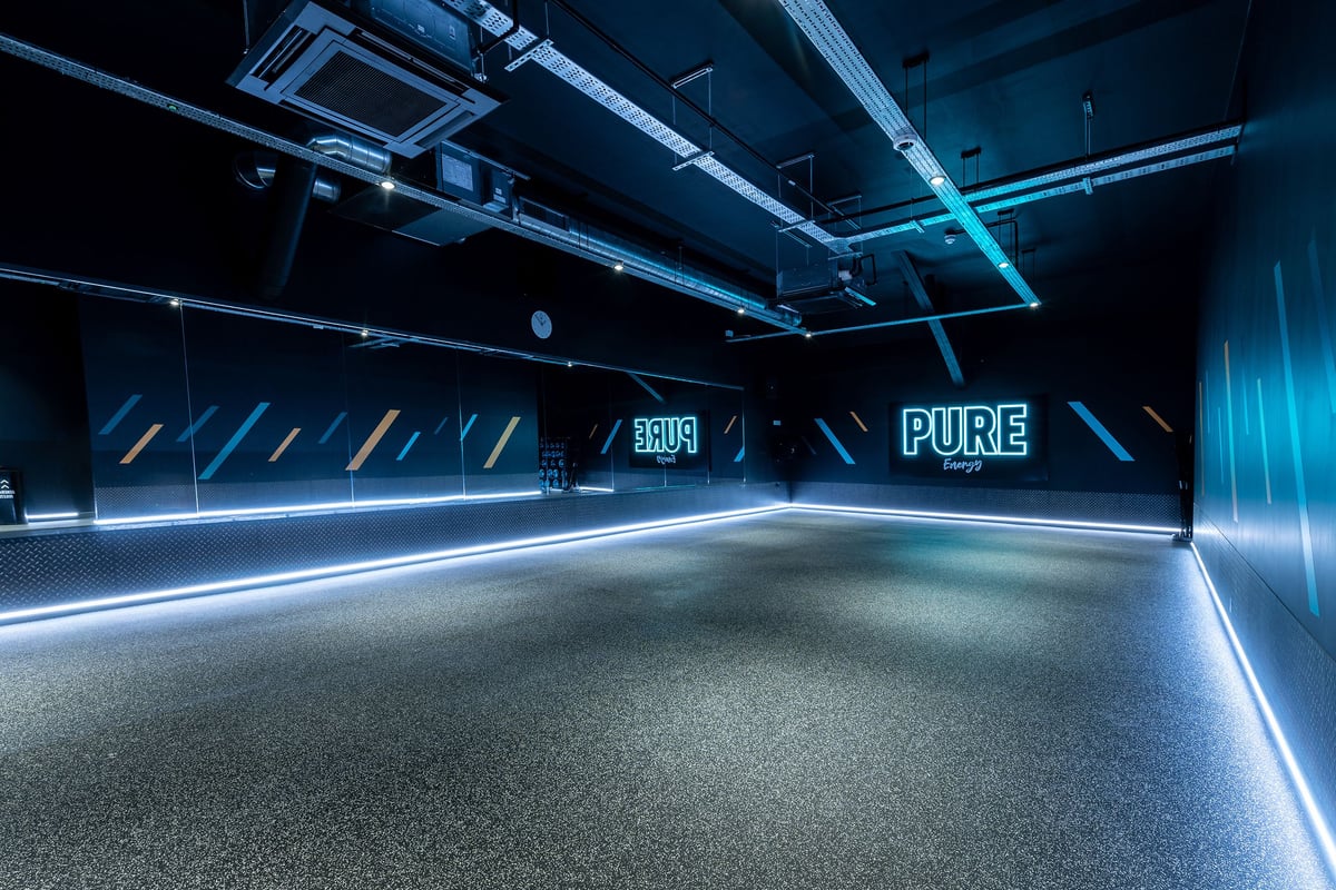 PureGym London Streatham: Dark studio with futuristic lighting, industrial style ceiling, and branded floor graphics.