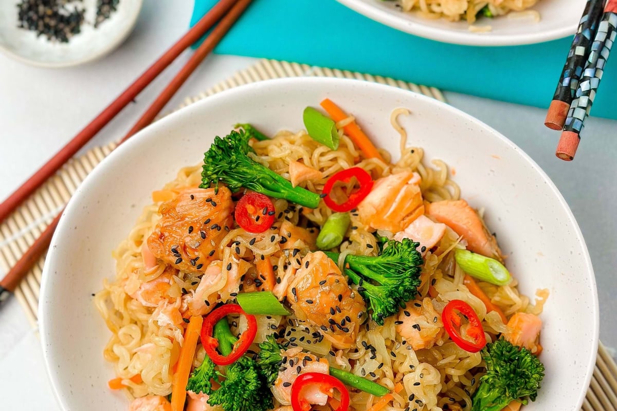 Noodles with salmon, broccoli, carrot, red chili, spring onion, and black sesame seeds in