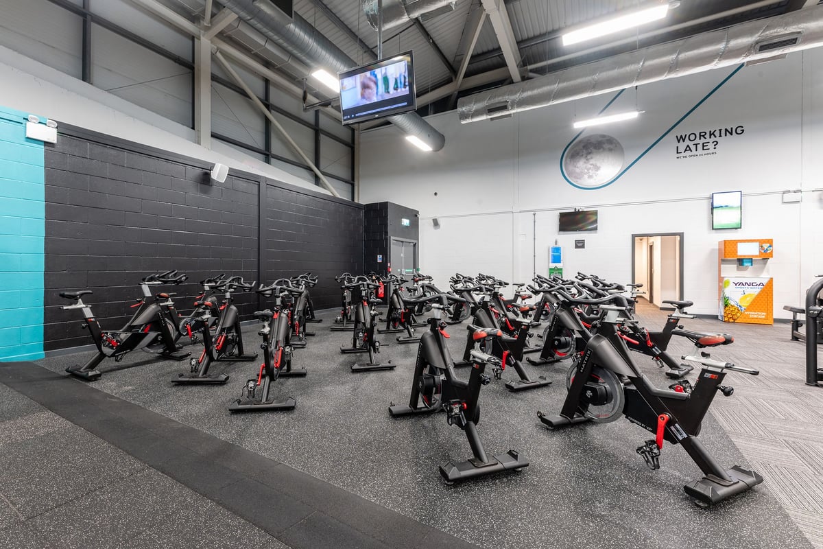 PureGym Birmingham West: Rows of stationary exercise bikes inside a well-lit gym with televisions and signage.