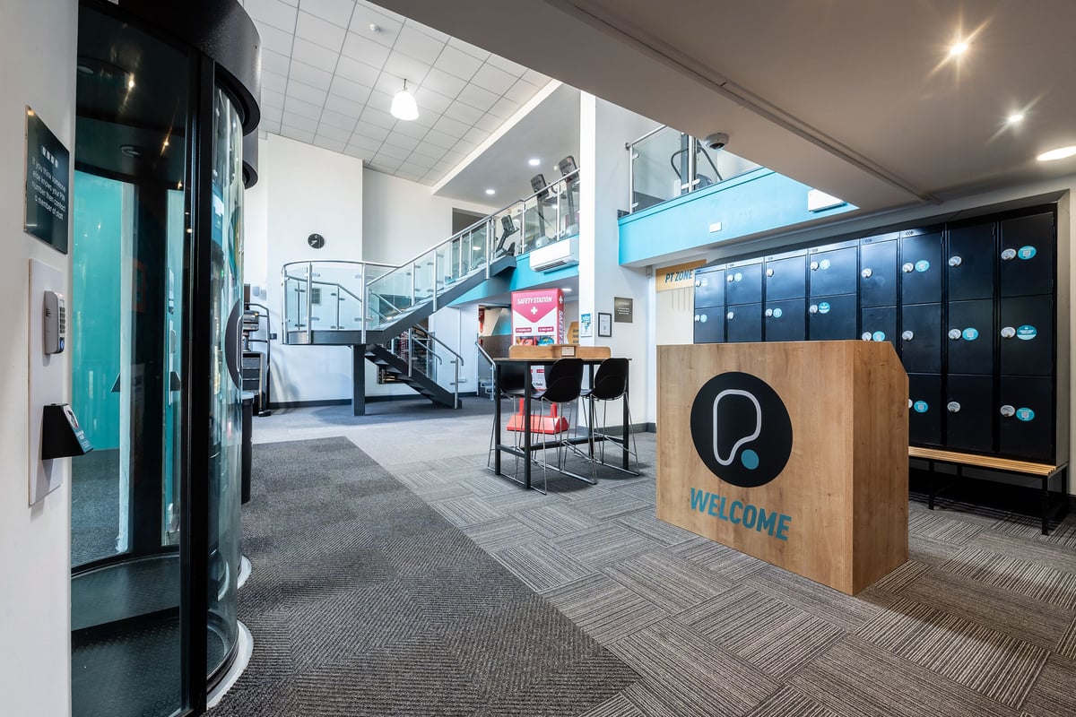 PureGym Sutton Coldfield: Lobby area with welcome sign, staircase, lockers, and seating nook.