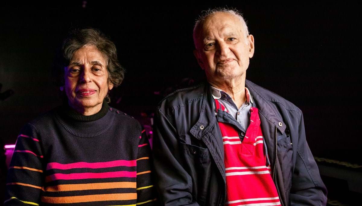 Elderly man and woman sitting side by side against a dark background