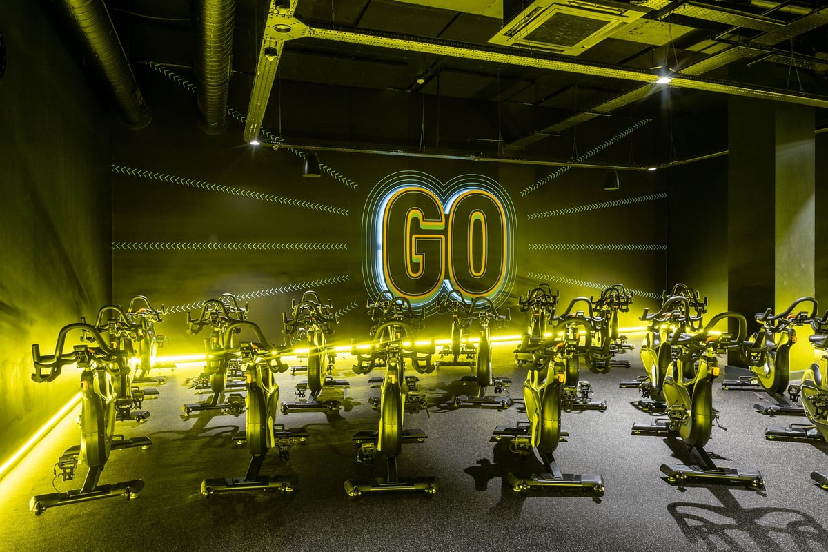 PureGym London Swiss Cottage: Rows of stationary bikes in neon-lit studio, 'GO' illuminated signage.