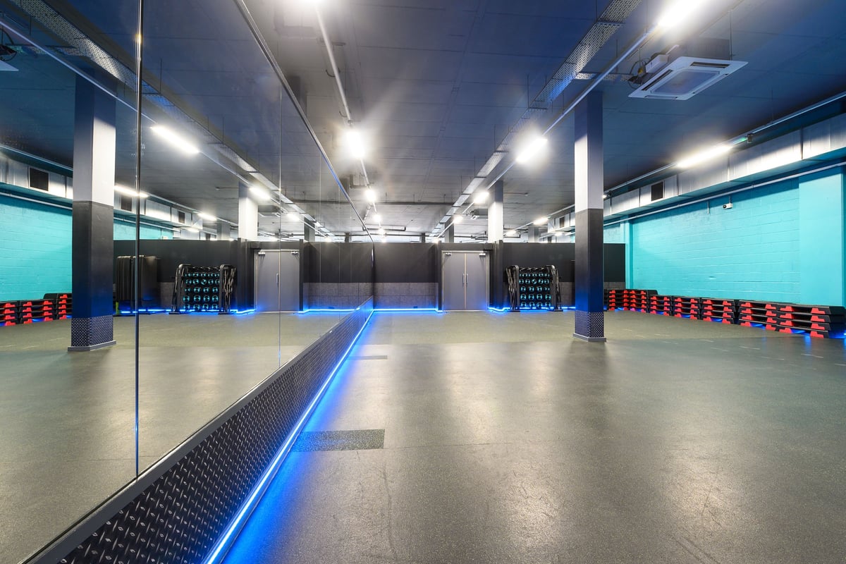 PureGym London Acton: Mirrored studio with weight racks, medicine balls, and blue accent lighting.