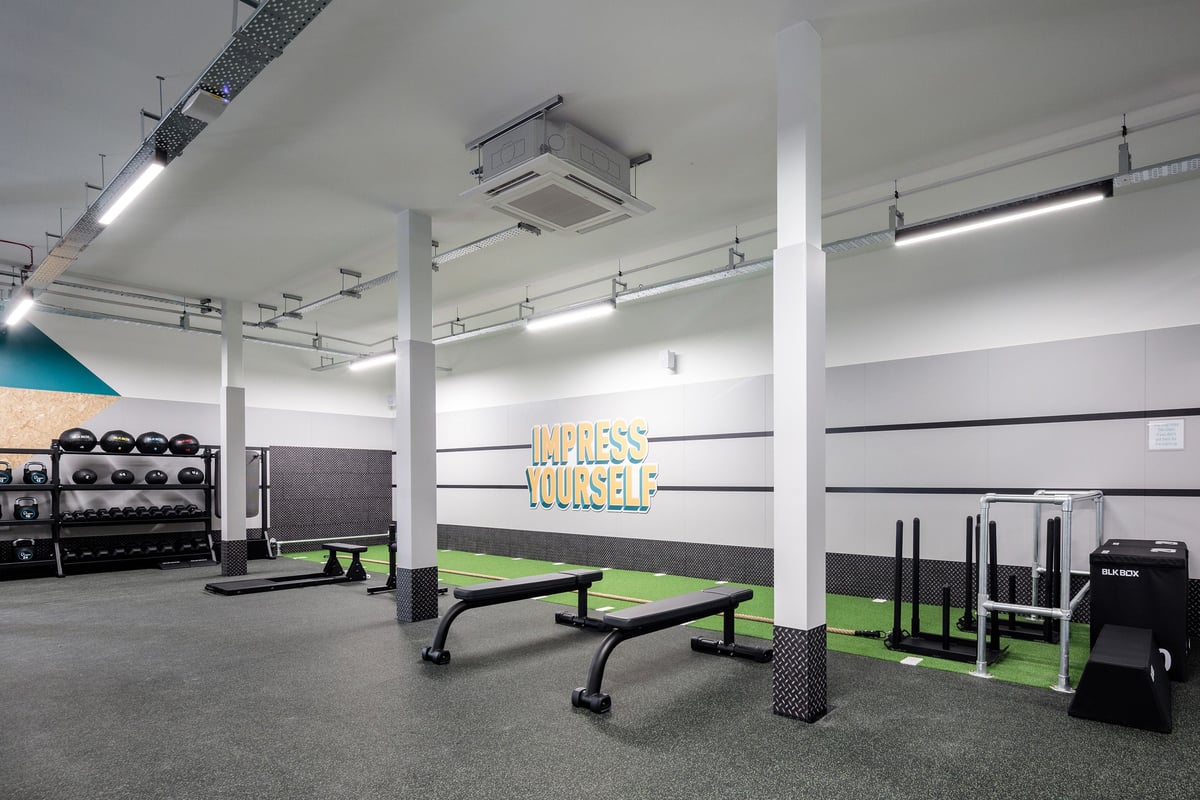 PureGym Frome: Weightlifting area with squat racks, benches, rubberized flooring, and weight plates.