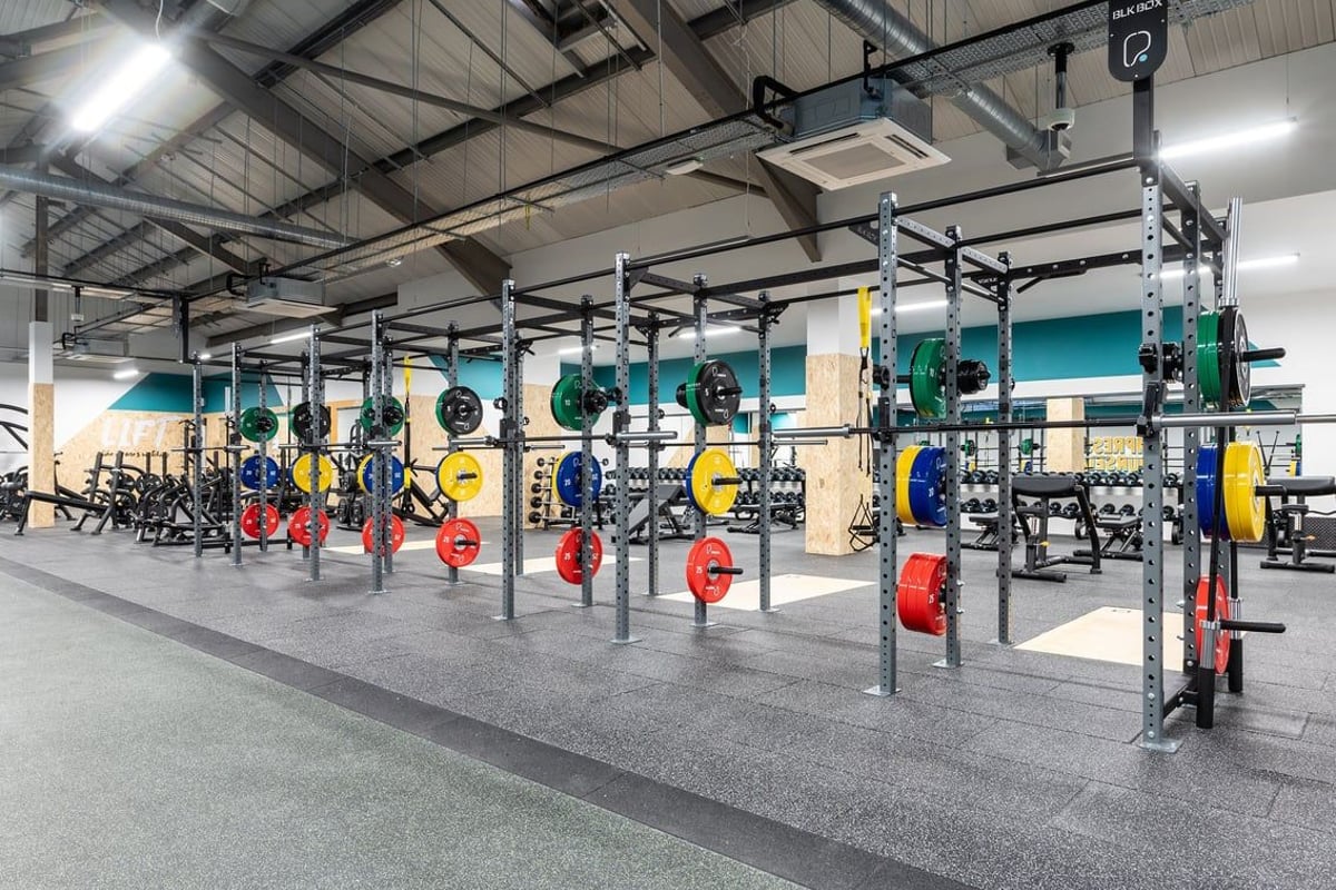 PureGym Derby Meteor Centre: Squat racks, weight plates, barbell stations in a gym weightlifting area.