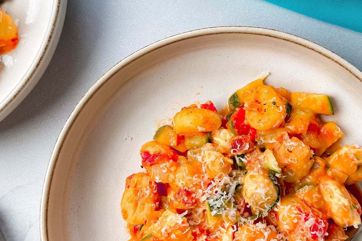 Gnocchi with vegetables and grated cheese served on a beige plate with a fork.