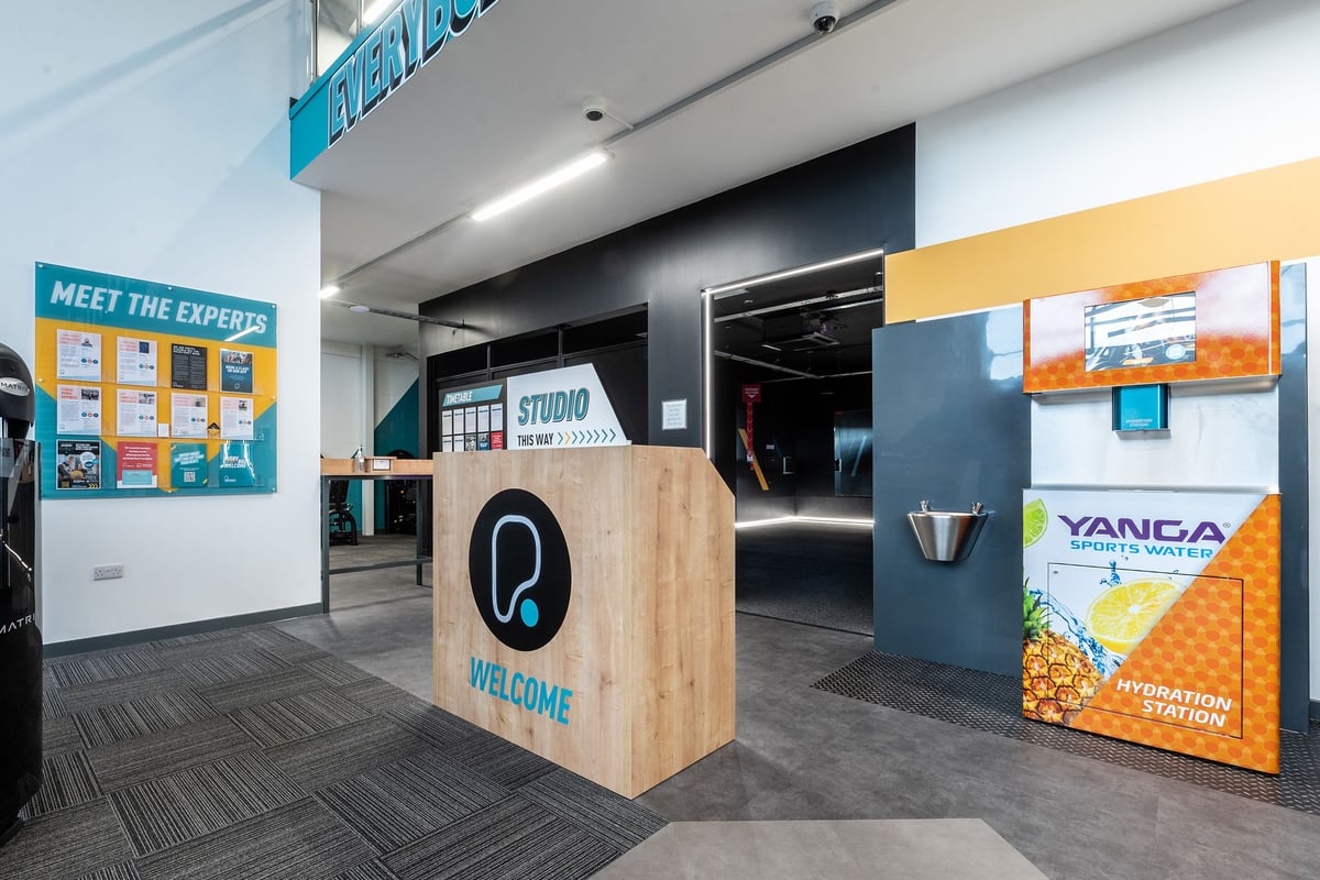 PureGym Trowbridge: Reception area with wooden front desk and branded wall signage.