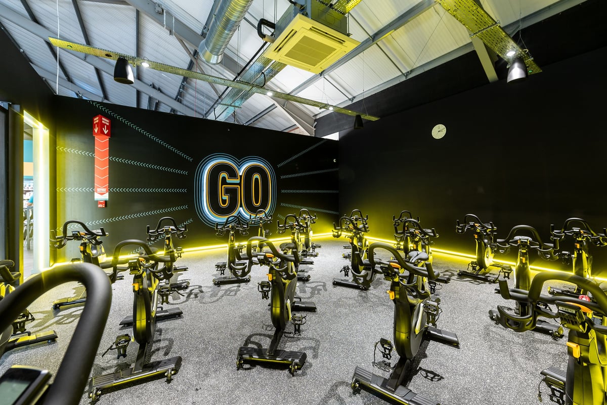 PureGym Derby Meteor Centre: Rows of stationary exercise bikes with neon "GO" lighting in a gym setting.