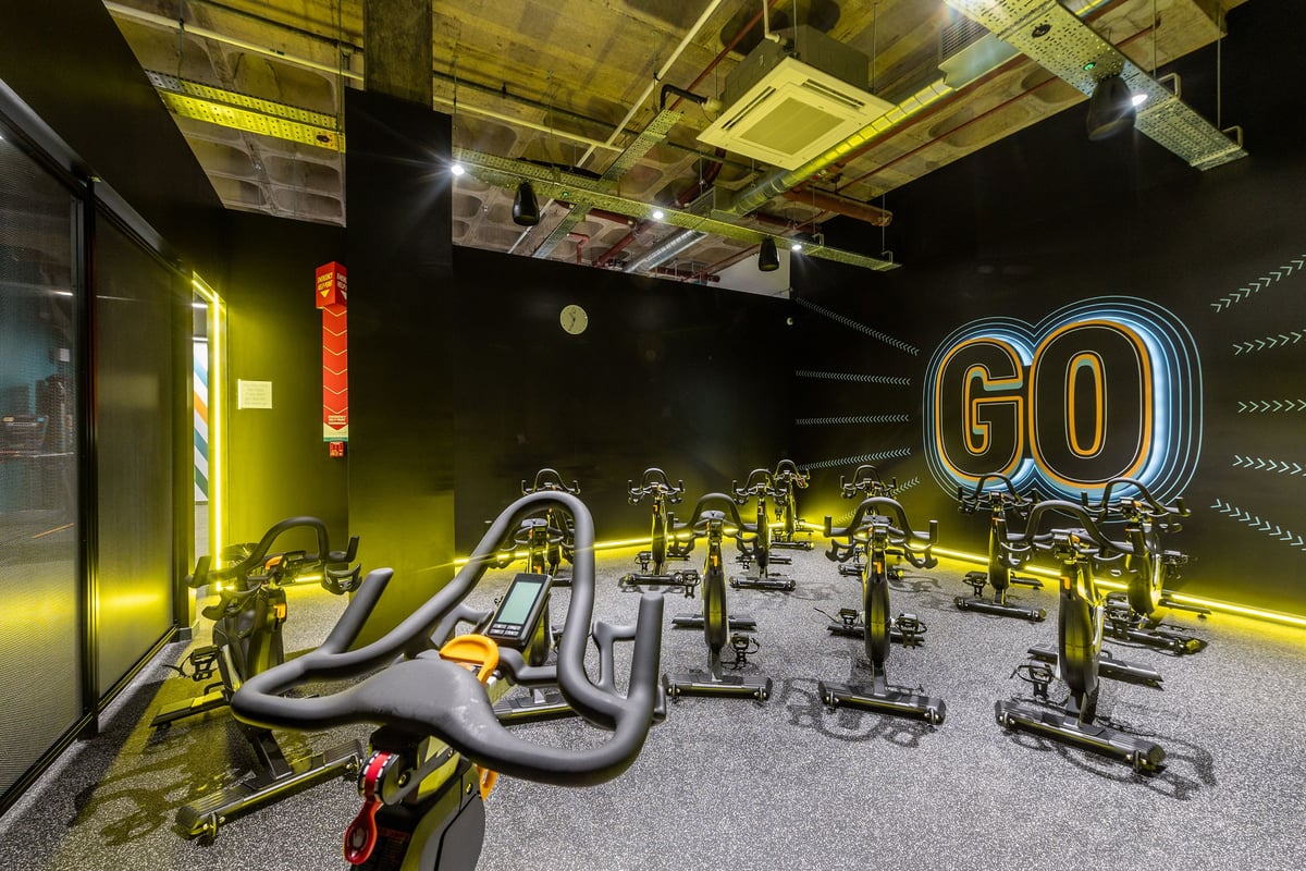 PureGym London Wood Green: Rows of futuristic stationary bikes with neon 'GO' sign in dimly lit studio.