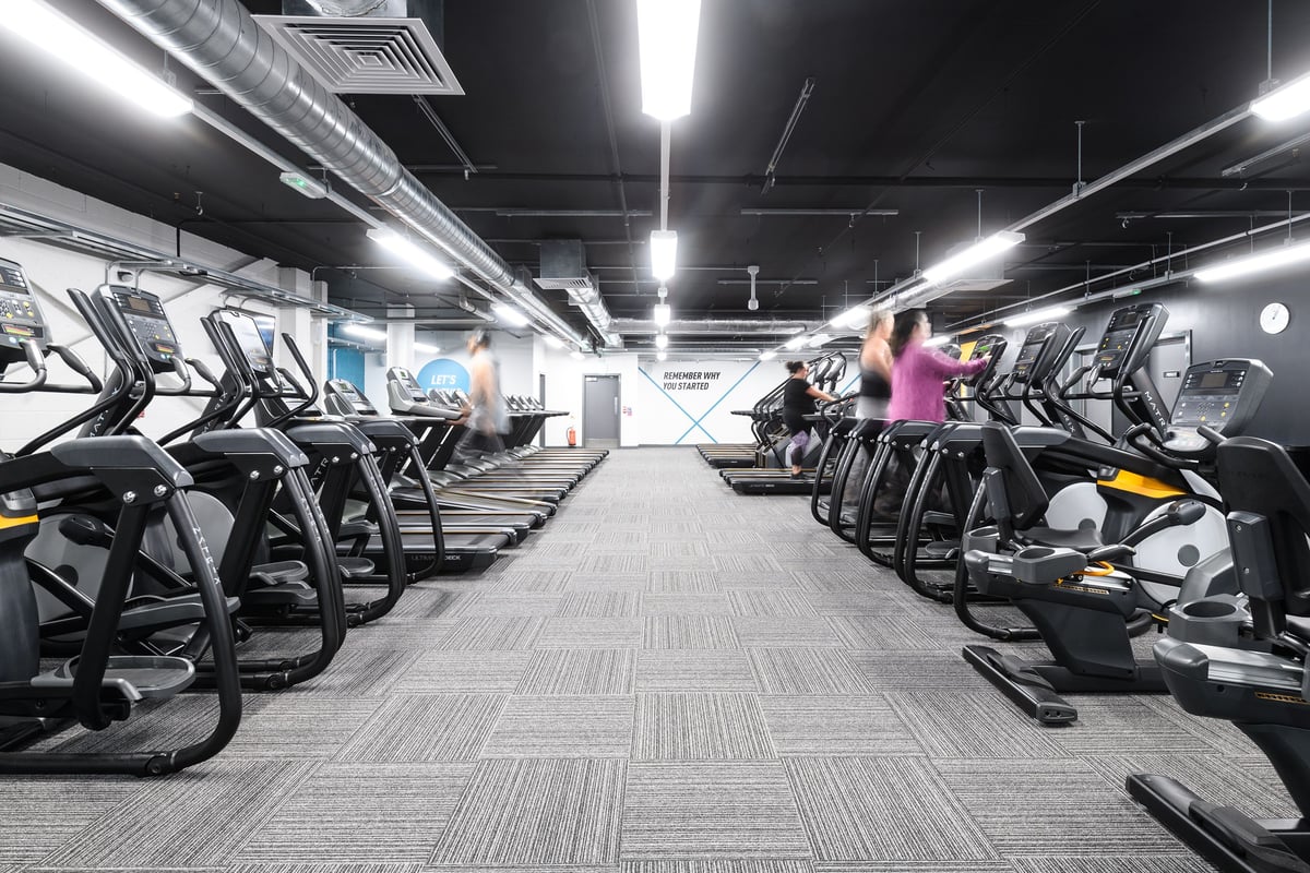 PureGym Glasgow Silverburn: Rows of treadmills, ellipticals, and exercise bikes in a dimly lit fitness centre.