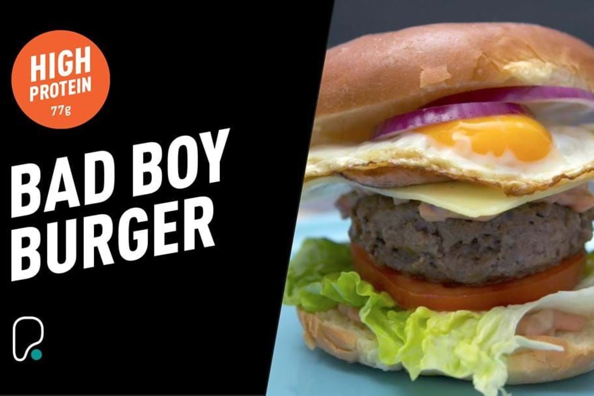 Burger with fried egg, cheese, tomato, lettuce, and red onion in a bun