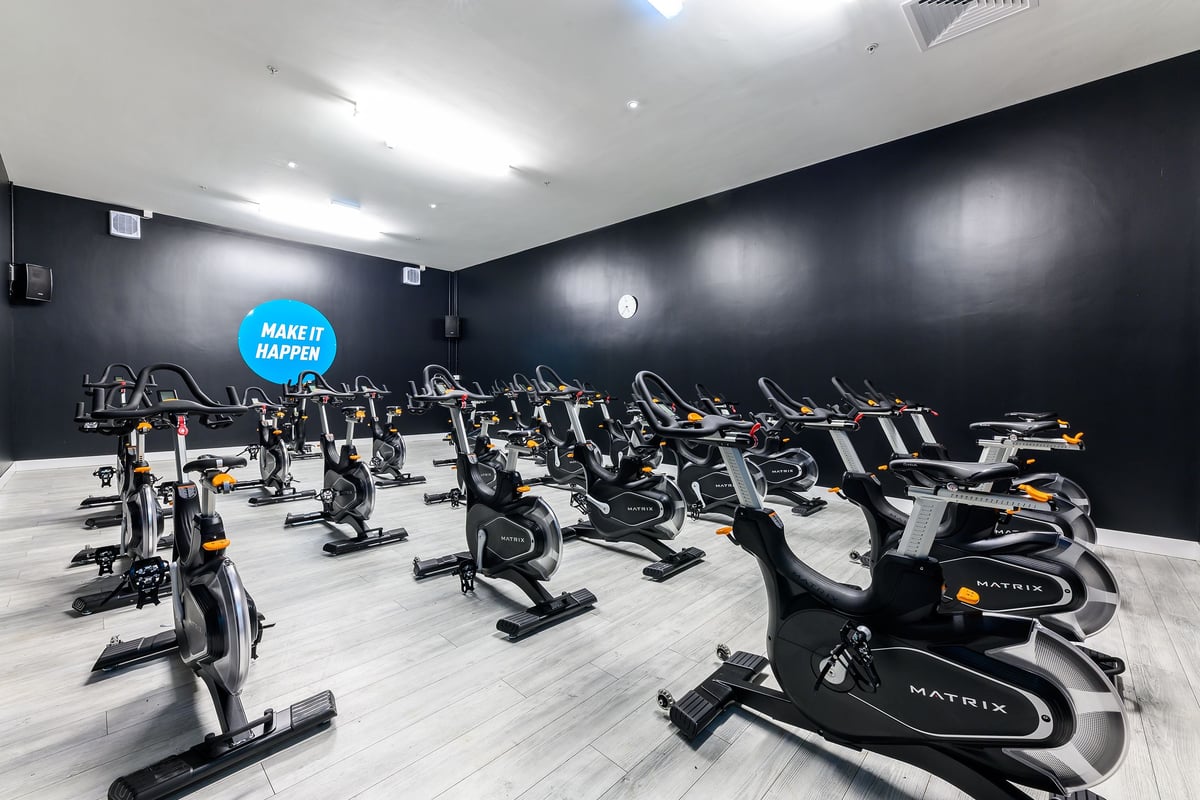 PureGym Wisbech: Rows of stationary bikes and ellipticals in a dimly lit studio with black walls.