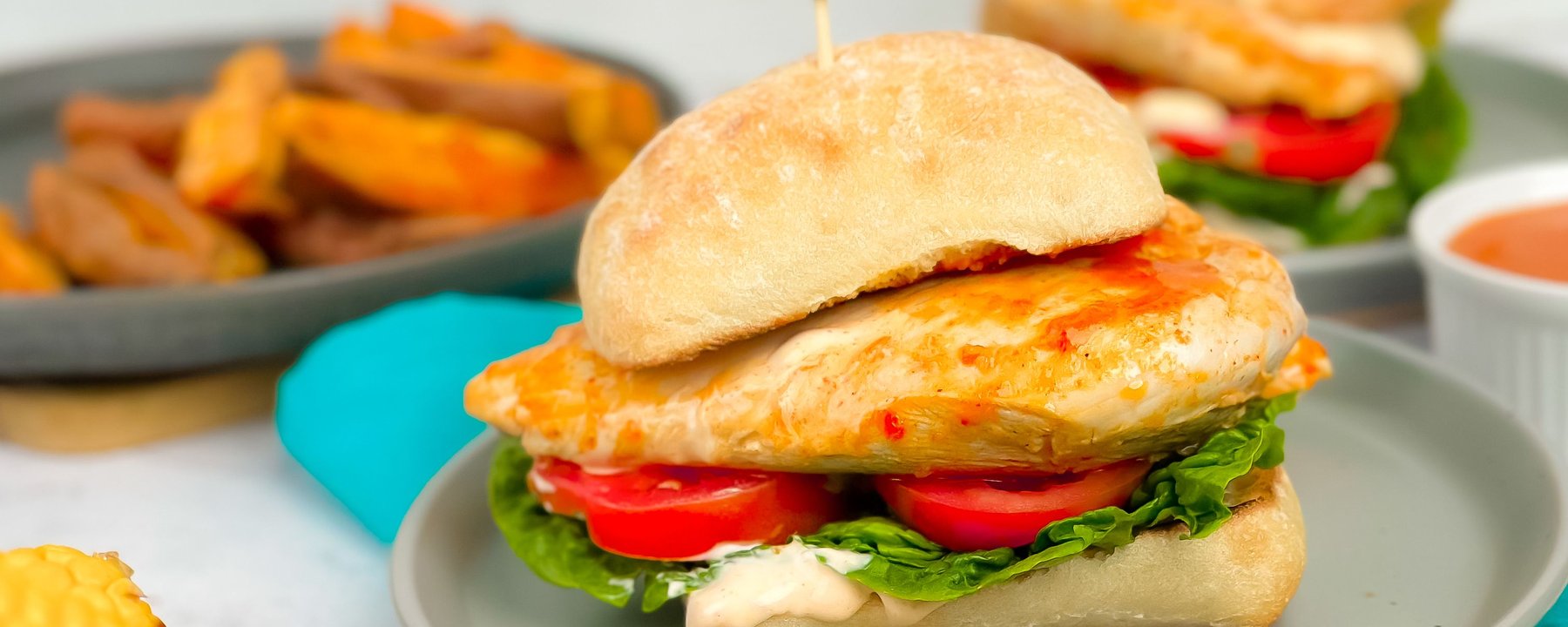 Grilled chicken burger with lettuce, tomato and sauce on a bun with chips on the side