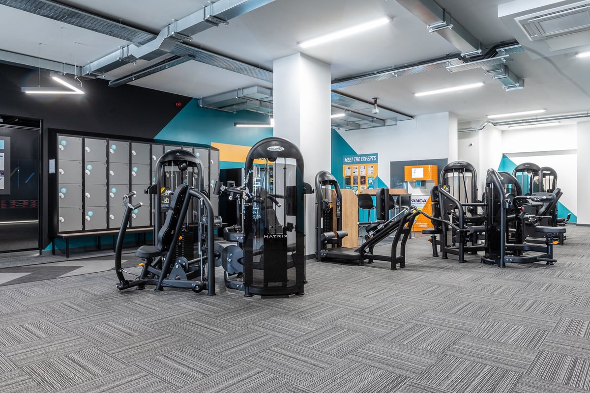 PureGym Coalville: Resistance machines, weight racks, benches, and rubberized flooring in a gym studio with teal accents.