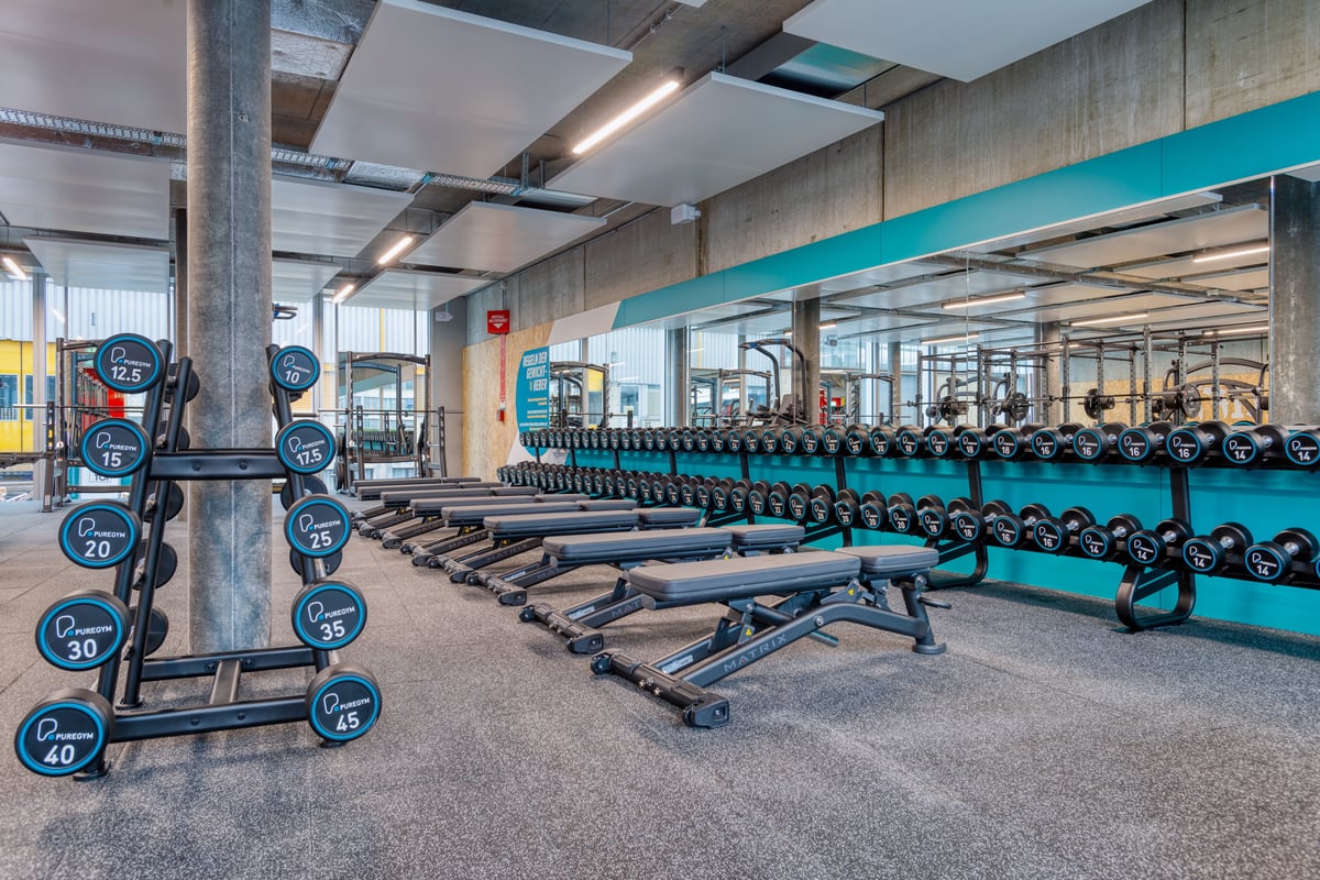 PureGym Zürich Oerlikon: Weitwinkelansicht des Freihantelbereichs mit Bänken, Kurzhanteln und Squat Racks.