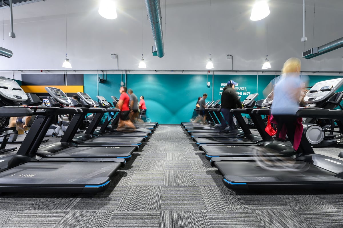 PureGym Bromsgrove Retail Park: Rows of treadmills inside a gym with teal accents and people exercising blurred in motion.