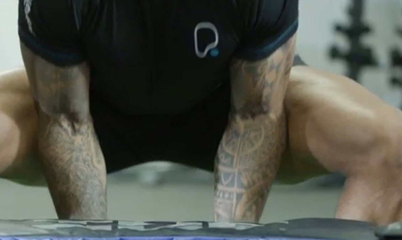 Tattooed arms and muscular legs of a person in a black shirt doing a workout.