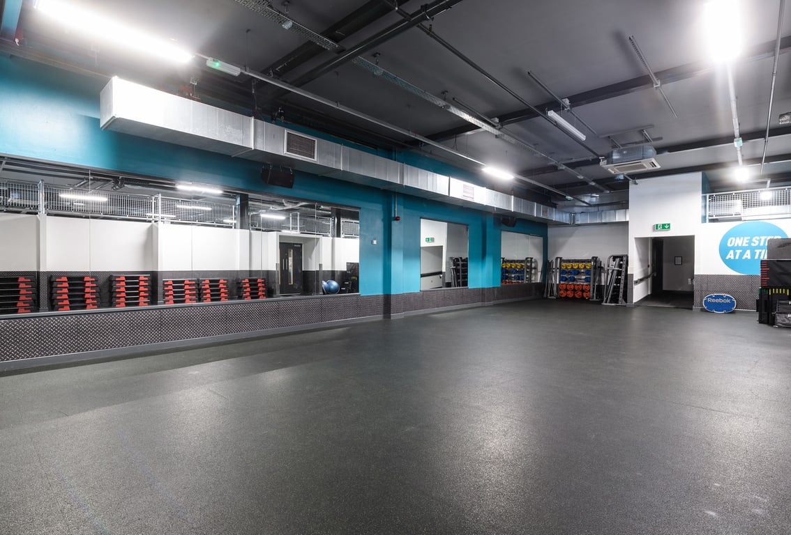 PureGym Bristol Harbourside: Gym studio with weight racks, free weights, rubberized floors, and teal accented walls.