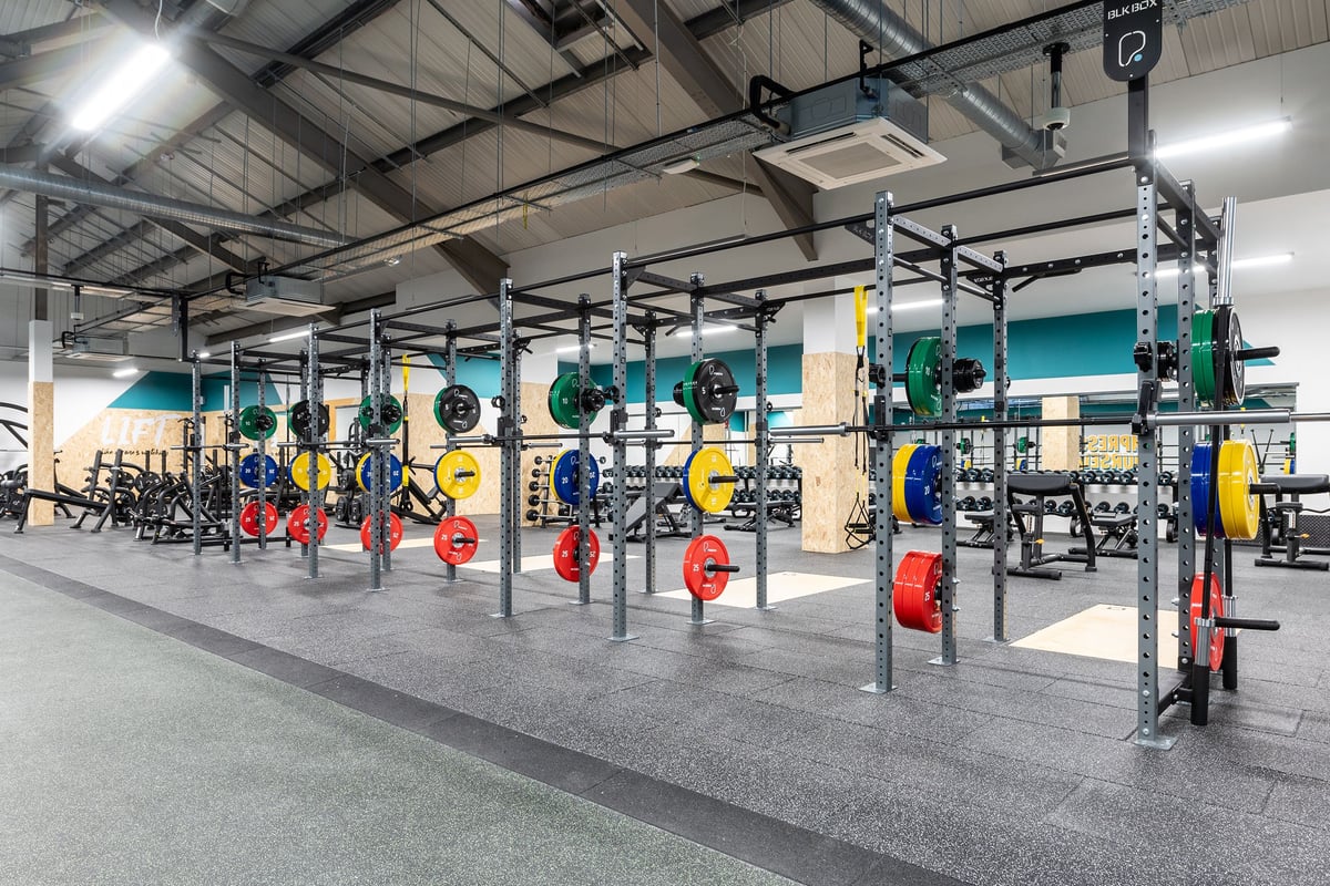 PureGym Derby Meteor Centre: Squat racks, weight plates, barbell stations in a gym weightlifting area.