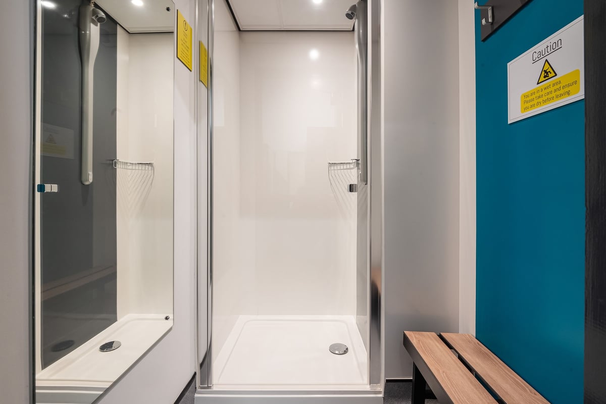 PureGym Linlithgow: Shower cubicles with tiled walls, glass doors, and benches.