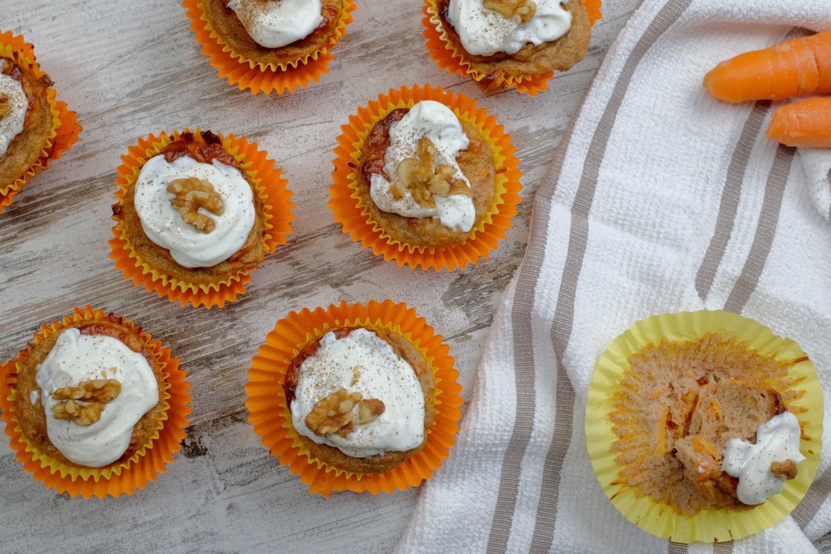 Seven carrot cake muffins with white icing and walnut toppings on a wooden surface