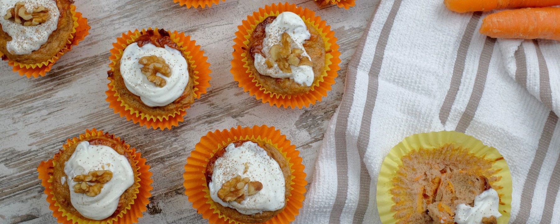 Seven carrot cake muffins with white icing and walnut toppings on a wooden surface