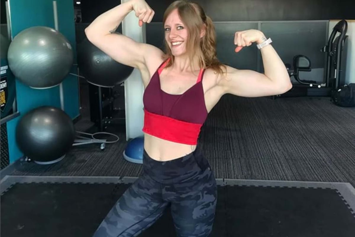 Woman in gym wear flexing biceps with exercise balls and equipment in background