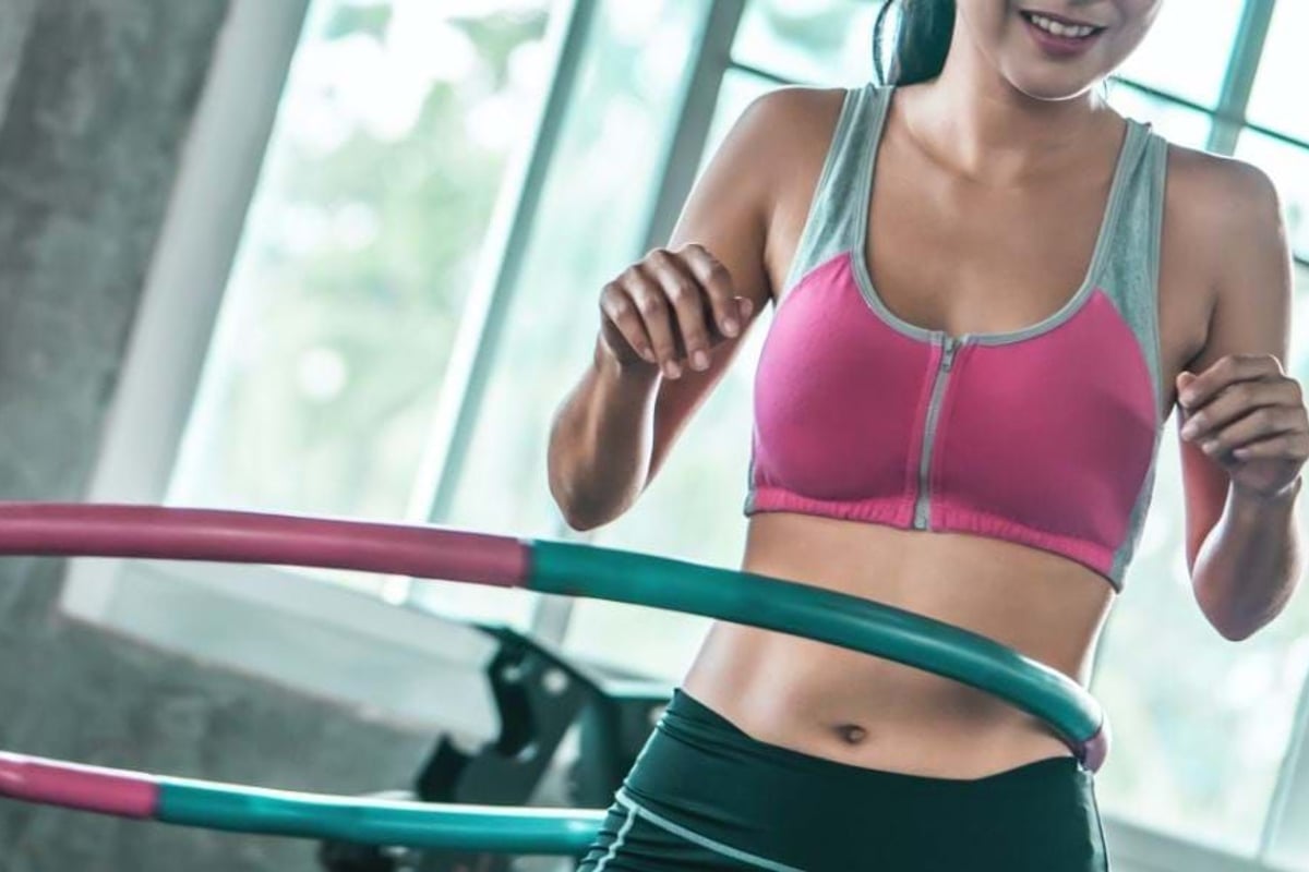 Woman in pink sports bra using a hula hoop indoors near large windows