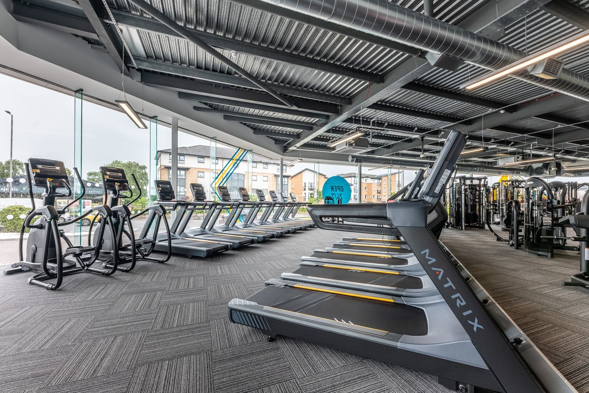 PureGym Glasgow Giffnock: Rows of treadmills, exercise bikes, and weight machines under a corrugated metal ceiling.