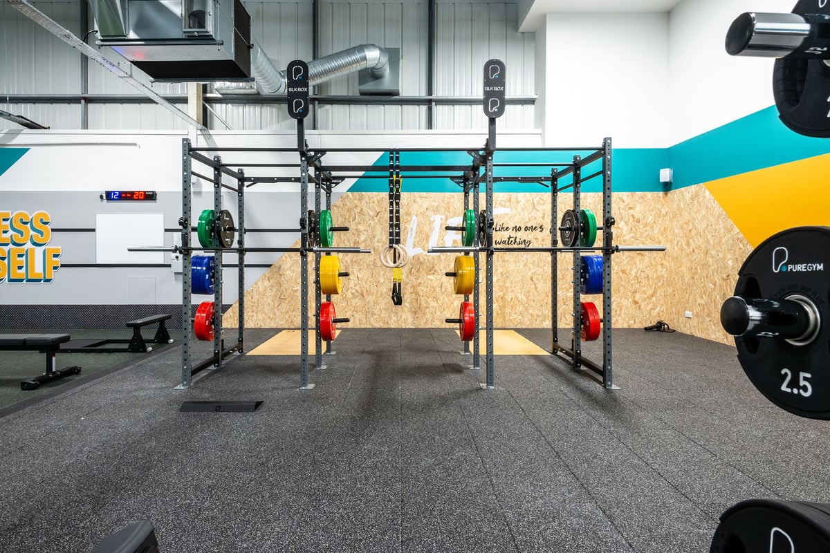 PureGym Oswestry: Squat racks, weight plates in various colours, rubberized flooring, mirrored wall.