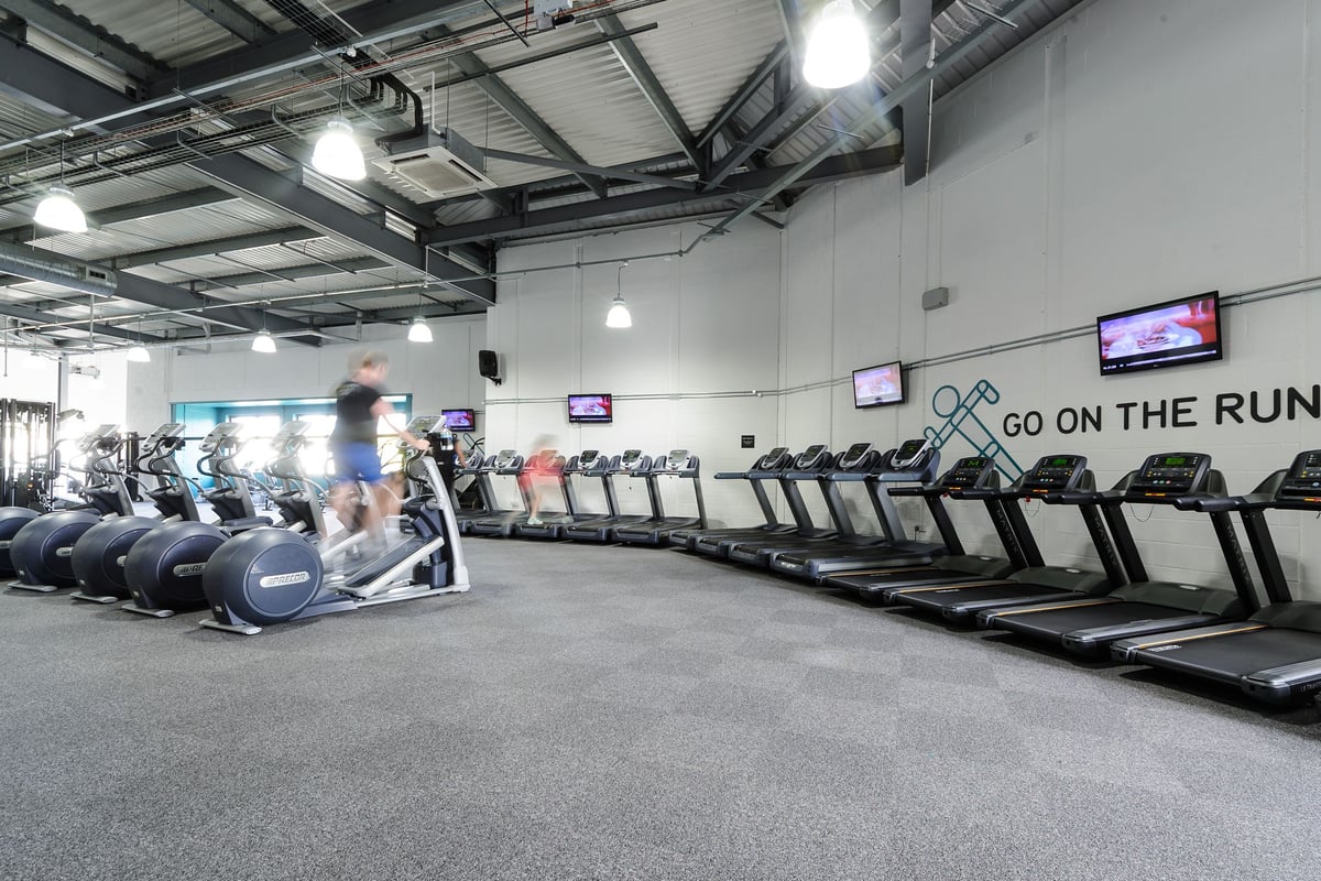 PureGym Worcester: Rows of treadmills and screens in a bright, industrial-style gym with ceiling-mounted lights.